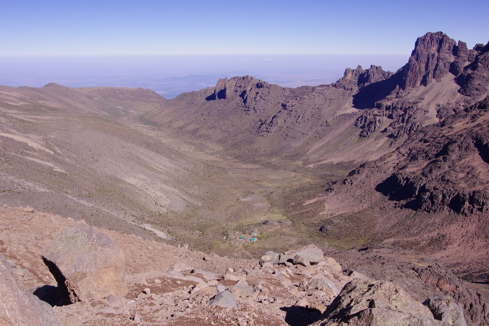 Wide panoramic view looking down a vast rocky valley on Mount Kenya beneath a clear sky.