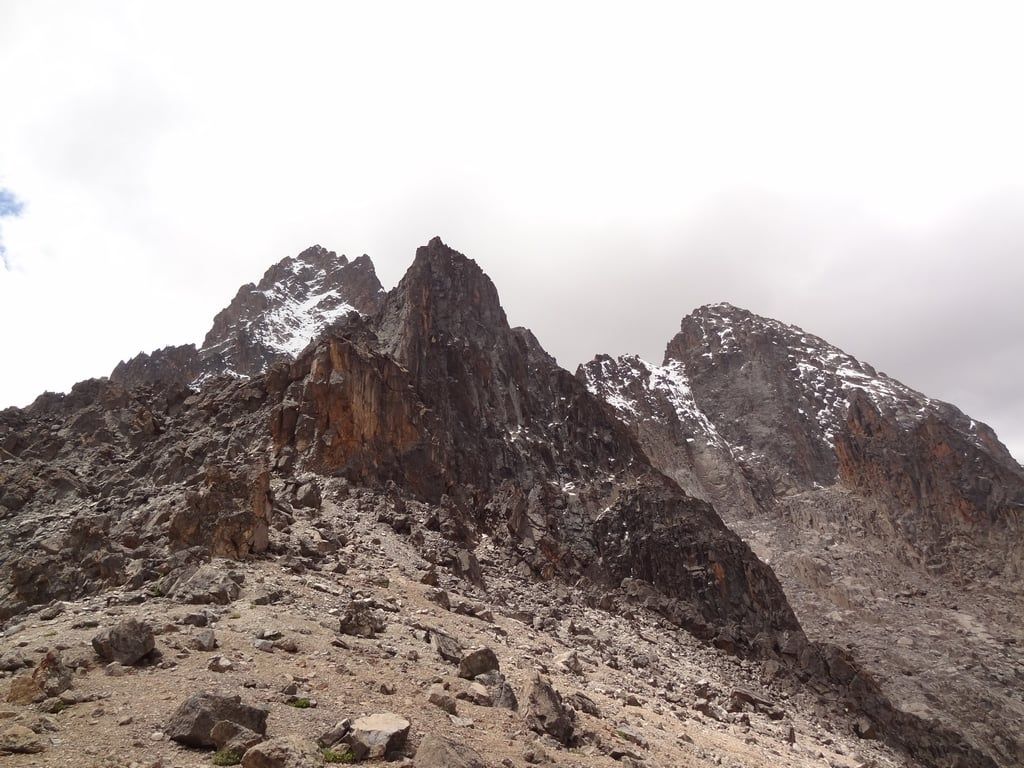 Rocky summit towers of Batian and Nelion rise above a boulder-strewn slope on Mount Kenya.
