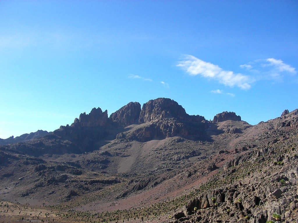 Rugged rocky peaks and high-altitude slopes of Mount Kenya rise under a clear blue sky.