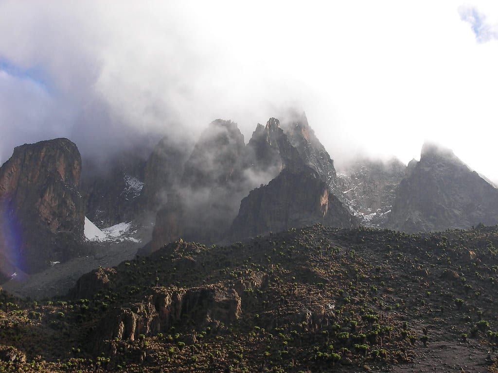 Rugged rocky peaks of Mount Kenya rise into dramatic mist and clouds above steep alpine slopes.