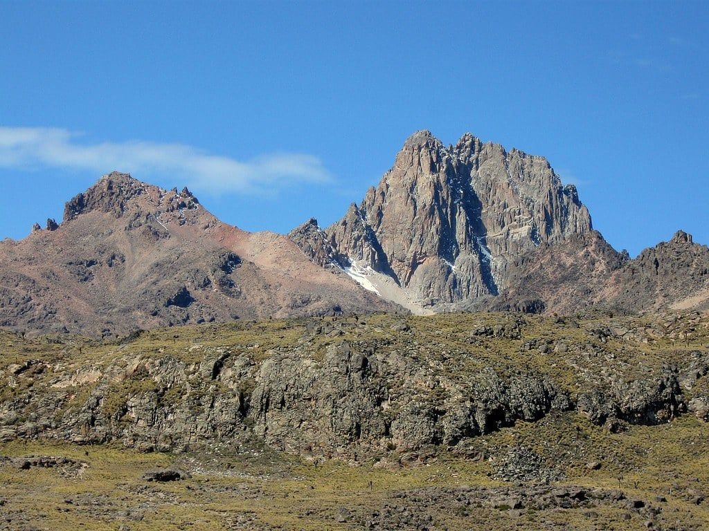 Point Lenana and the rocky summits of Mount Kenya rise above the moorland under a clear blue sky.