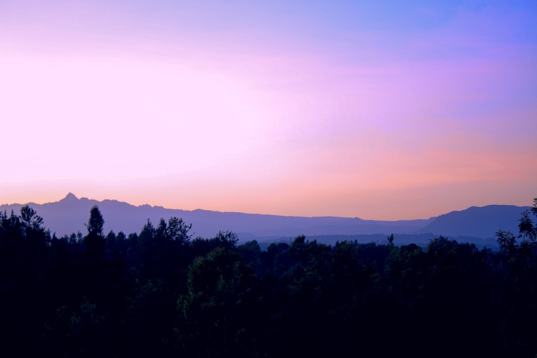 Silhouette of Mount Kenya along the horizon under a gradient purple and pink sunset sky.